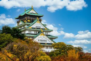 Osaka Castle seen above autumn trees under blue sky