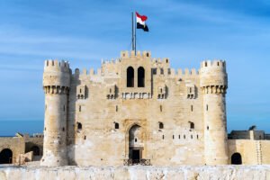 Front façade of Qaitbay Citadel with Egyptian flag against blue sky