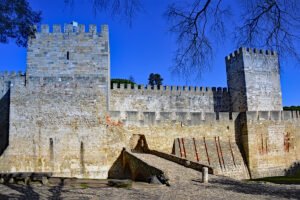 View of São Jorge Castle stone walls, arched bridge and battlements against clear blue sky