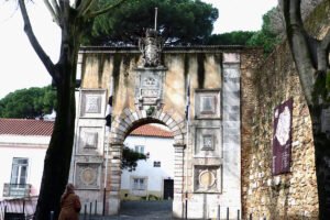 Stone arched gate of São Jorge Castle with trees and visitor in foreground