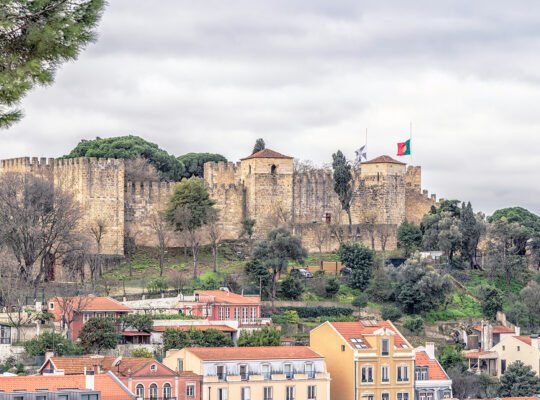 View of São Jorge Castle atop tree-lined hill above Lisbon rooftops