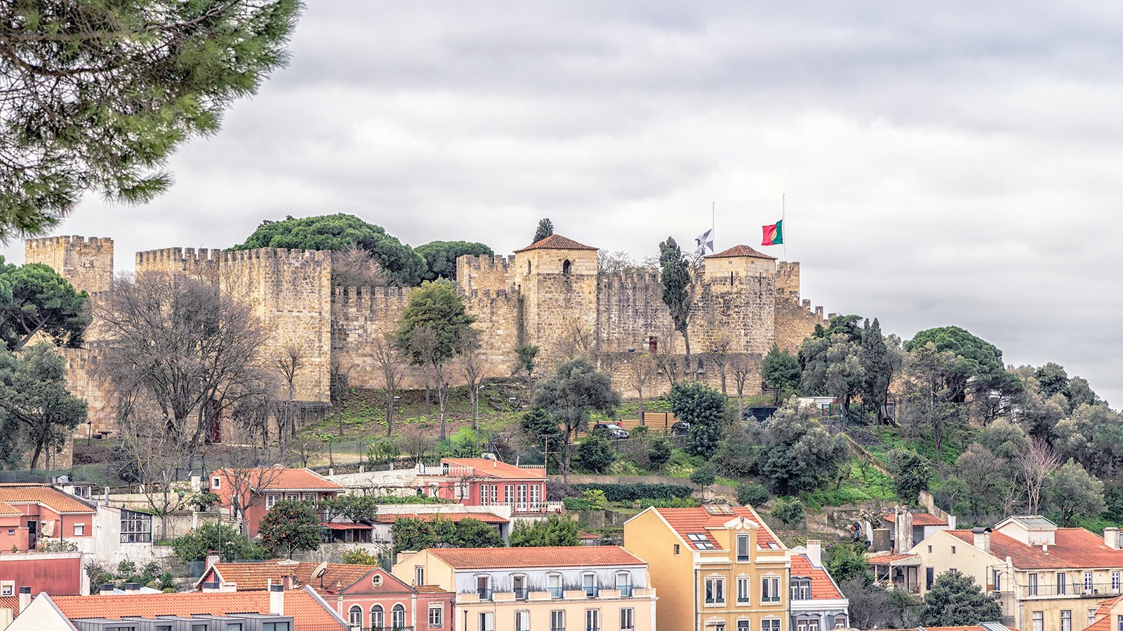 View of São Jorge Castle atop tree-lined hill above Lisbon rooftops