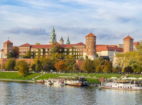 Wawel Castle on riverbank with boats and autumn trees