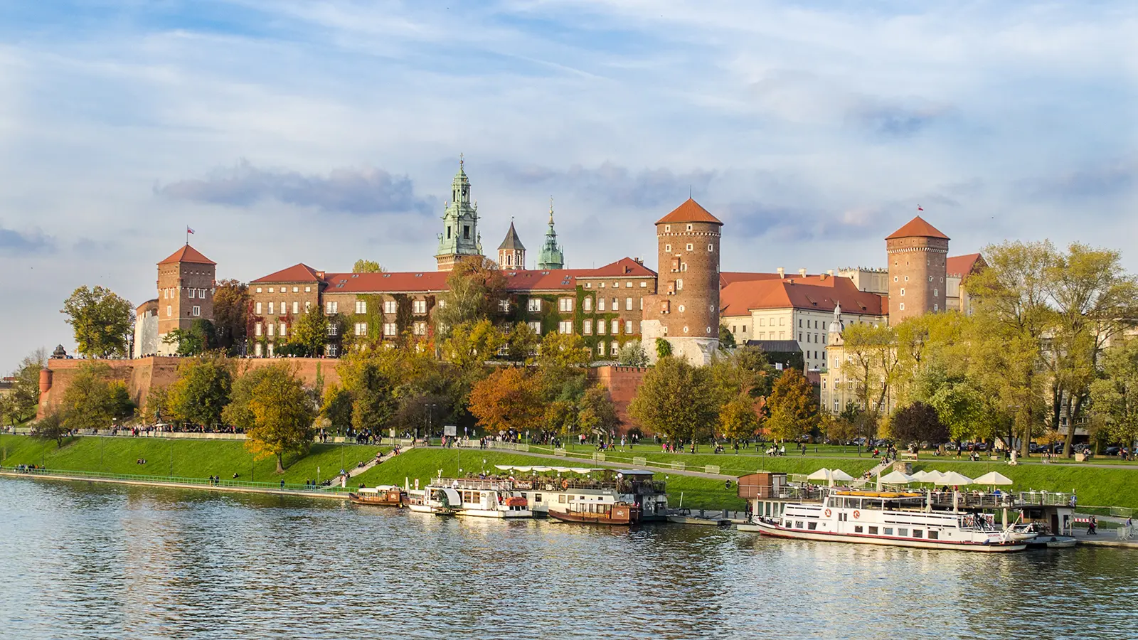 Wawel Castle on riverbank with boats and autumn trees