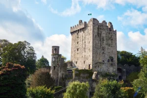 Blarney Castle stone tower rising above leafy gardens under a blue sky