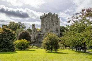 Blarney Castle stone tower amid green lawns and trees under cloudy sky