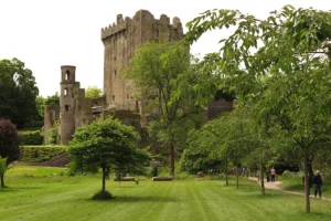 Blarney Castle stone tower with green lawns, trees, and visitors on a walking path