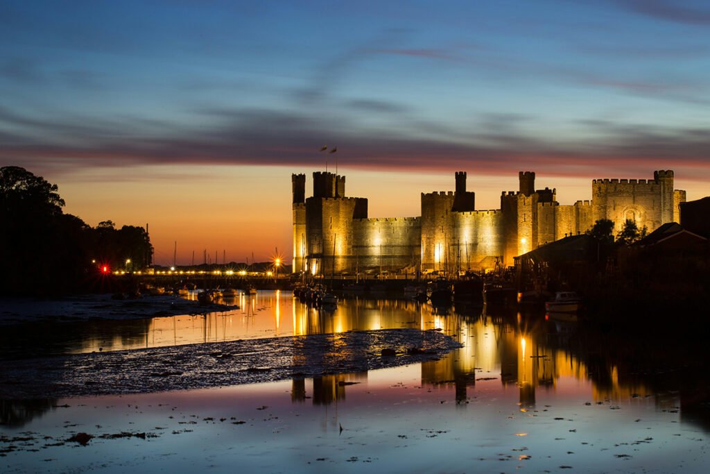 Caernarfon Castle lit at sunset reflected in estuary