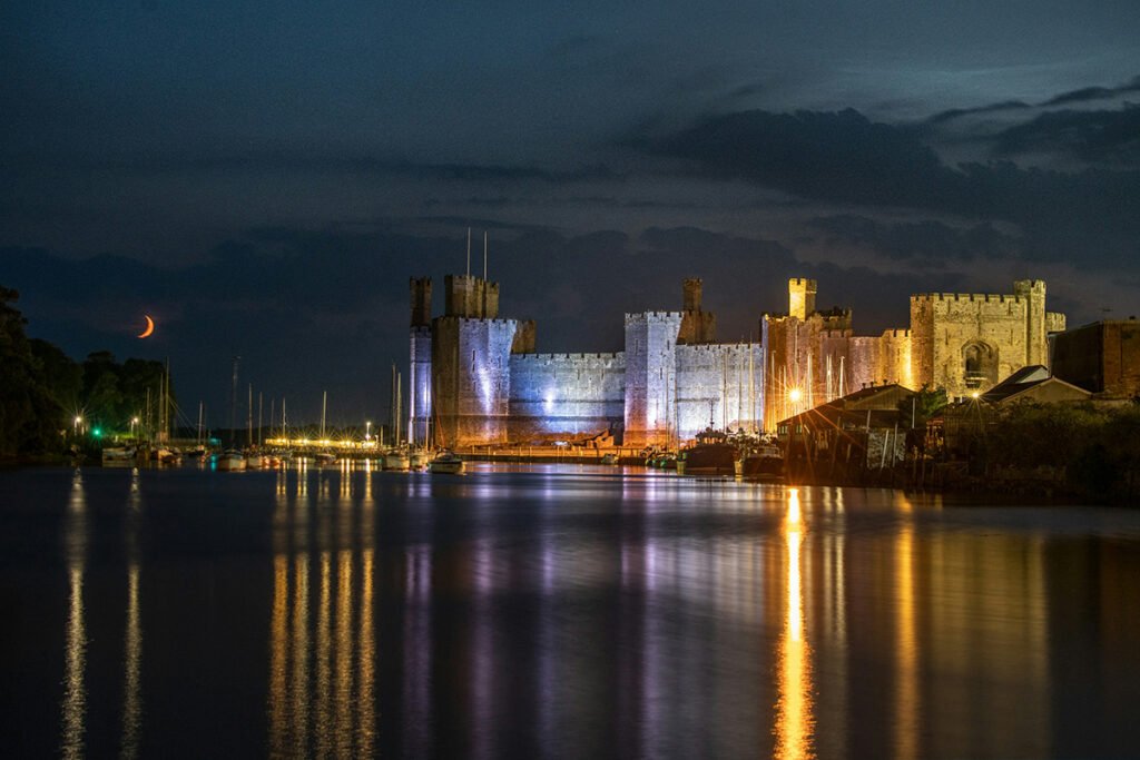 Illuminated Caernarfon Castle reflected on river at night