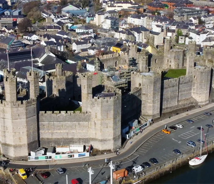 Aerial view of Caernarfon Castle with town and harbour in sunlight.