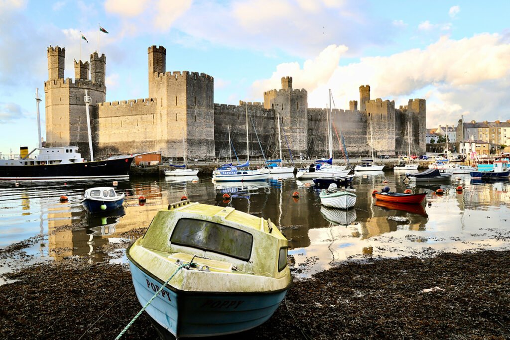 View of Caernarfon Castle across harbour with moored boats and reflected stone walls