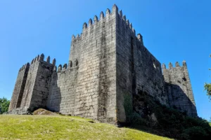 Castle of Guimaraes seen from grassy slope against blue sky