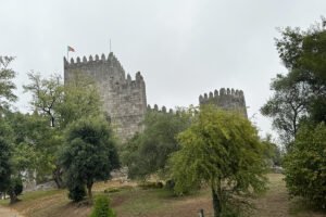 Stone towers of the Castle of Guimaraes framed by trees under grey sky