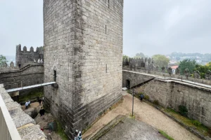 View of Castle of Guimaraes tower and battlements on overcast day, visitors on walkway