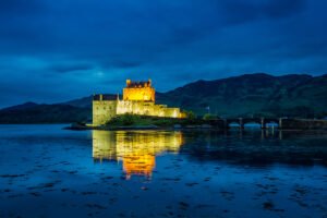 Eilean Donan Castle lit at twilight, reflected in loch waters