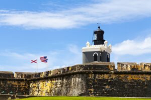 El Morro lighthouse above weathered fort walls with flags against blue sky