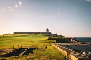 El Morro fortress on grassy headland with ocean and people walking at sunset
