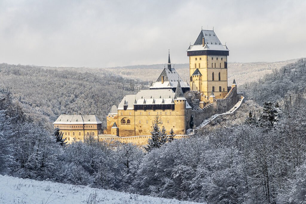 Snow-dusted Karlštejn Castle perched above frosted Bohemian forest at dawn
