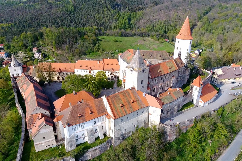Aerial view of Křivoklát Castle surrounded by forested hills and red-roofed buildings