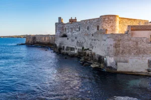 Maniace Castle fortress walls meeting the Ionian Sea at sunset