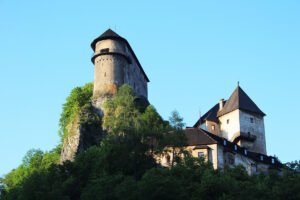 Orava Castle on rocky hilltop above trees, clear blue sky