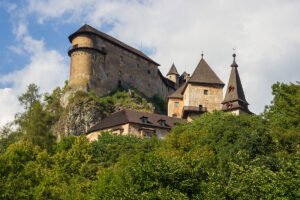 Orava Castle on rocky hill above green trees