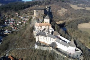 Aerial view of Orava Castle perched on rocky ridge above river and village