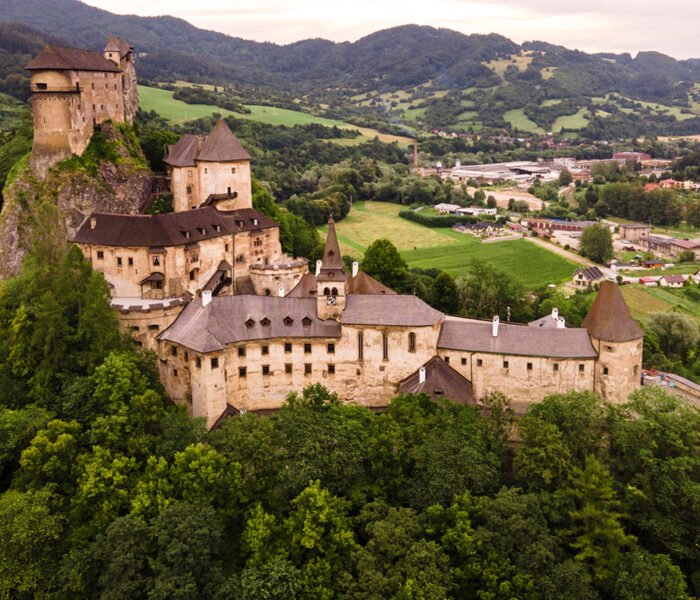 Aerial view of Orava Castle perched on rocky hill above forest and village