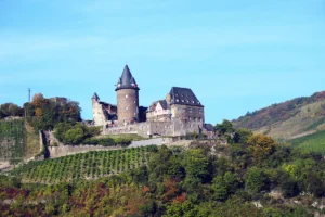 Stahleck Castle perched above vineyard-covered Rhine valley under blue sky