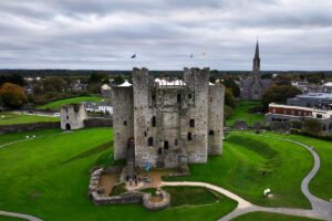 Aerial view of Trim Castle's stone keep and surrounding green banks under cloudy sky
