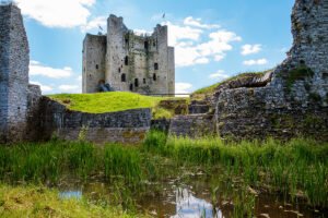 Trim Castle stone keep beyond moat and grassy ramparts under blue sky