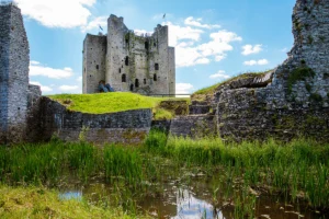 Trim Castle stone keep beyond moat and grassy ramparts under blue sky