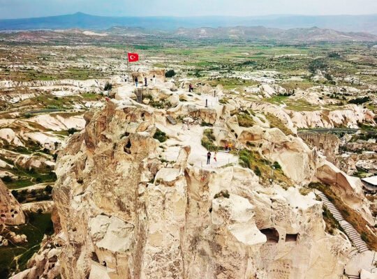 Aerial view of Uçhisar Castle overlooking Cappadocia valley with Turkish flag