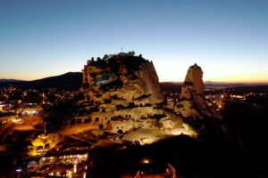 Uçhisar Castle illuminated at dusk above Cappadocia village