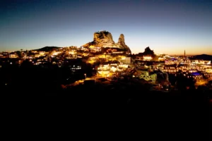 Uçhisar Castle illuminated above Cappadocia town at dusk