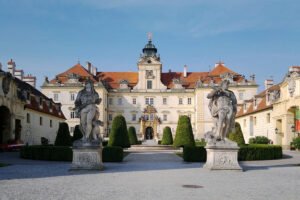 Front view of Valtice Castle with statues and formal gardens under blue sky