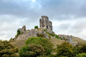 Corfe Castle ruins perched on a grassy Dorset hill under cloudy sky