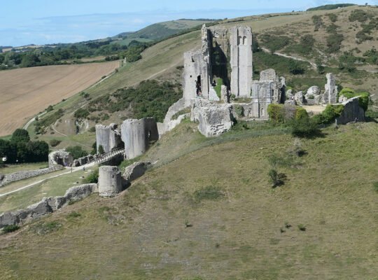 Aerial view of Corfe Castle ruins atop grassy hill