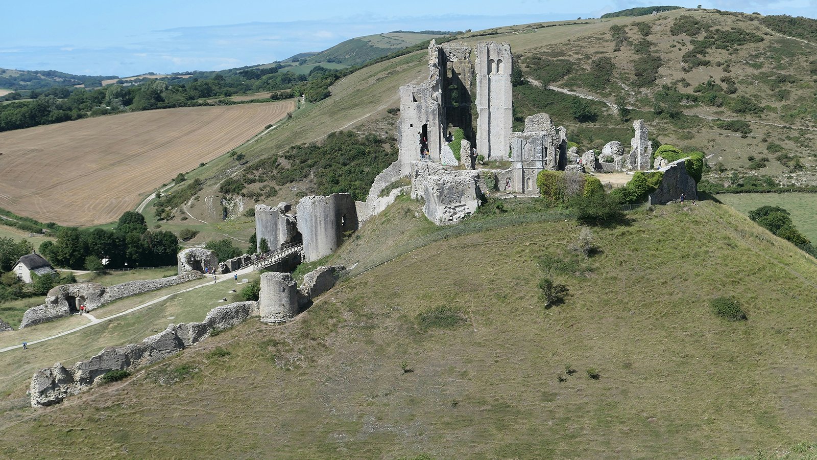 Aerial view of Corfe Castle ruins atop grassy hill