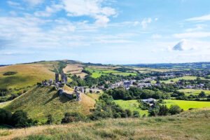 Ruined Corfe Castle on grassy hill with surrounding village and rolling Dorset countryside