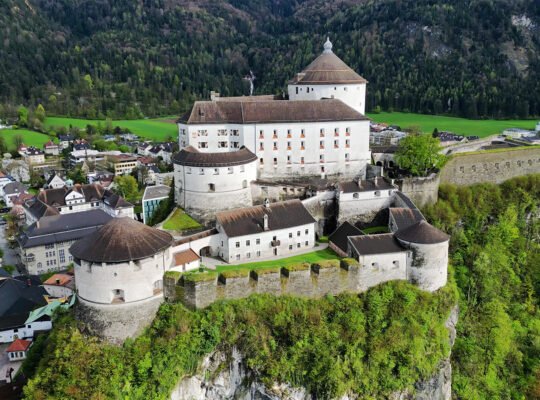 Aerial view of Kufstein Fortress perched on cliff above town and green forested valley