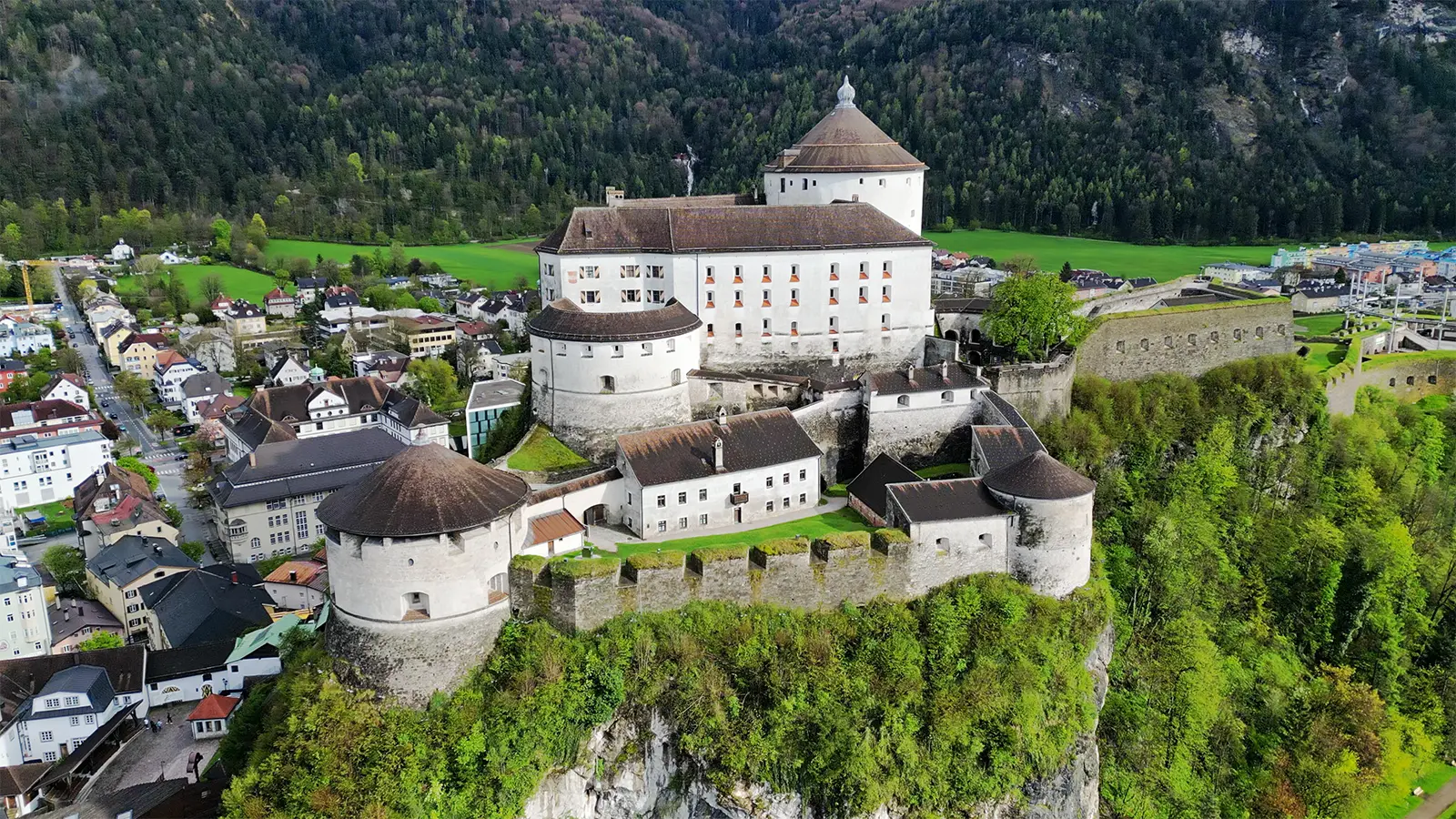 Aerial view of Kufstein Fortress perched on cliff above town and green forested valley