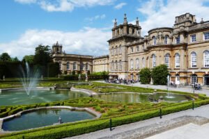 Blenheim Palace facade with formal fountains and gardens under blue sky