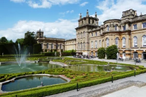 Blenheim Palace facade with formal fountains and gardens under blue sky