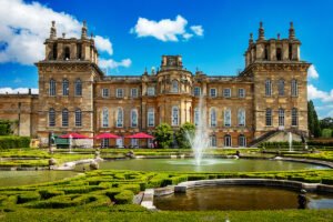 Blenheim Palace front facade with fountain and formal gardens on sunny day