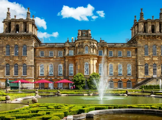 Fachada do palácio com fontes e jardins formais sob céu azul