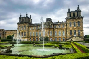 Blenheim Palace façade with fountains and formal gardens under cloudy sky