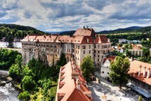 Cesky Krumlov Castle perched above river, red roofs and forested hills