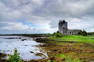 Dunguaire Castle beside tidal shoreline under cloudy sky