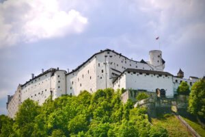 View of Fortress Hohensalzburg atop green hill under cloudy sky